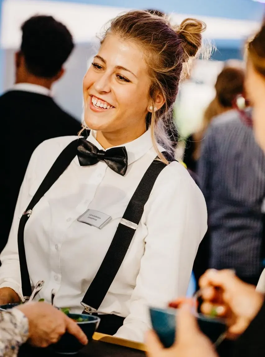 Lächelnde Servicemitarbeiterin umsorgt Gäste mit Fingerfood