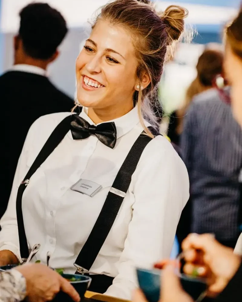 Lächelnde Servicemitarbeiterin umsorgt Gäste mit Fingerfood